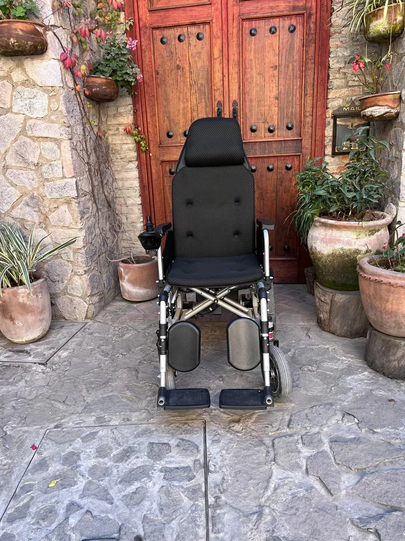 Silla eléctrica Ródano de frente, sobre el empedrado de un patio con portón de madera y macetas